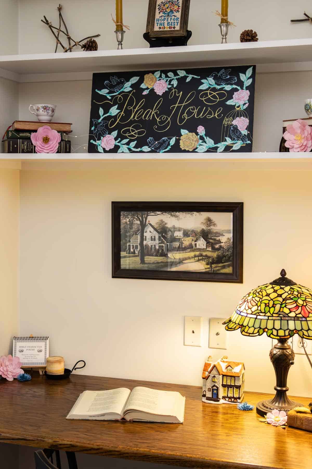 chalk sign saying "Bleak House" on a shelf with books and flowers.
